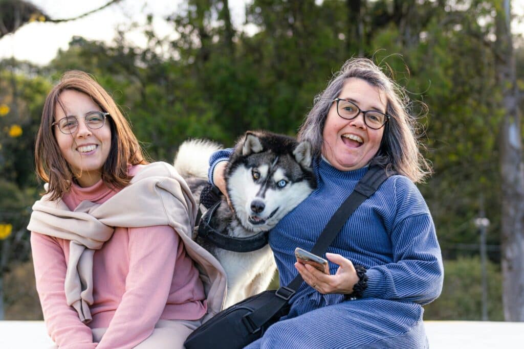 Two women and a husky dog smiling outdoors